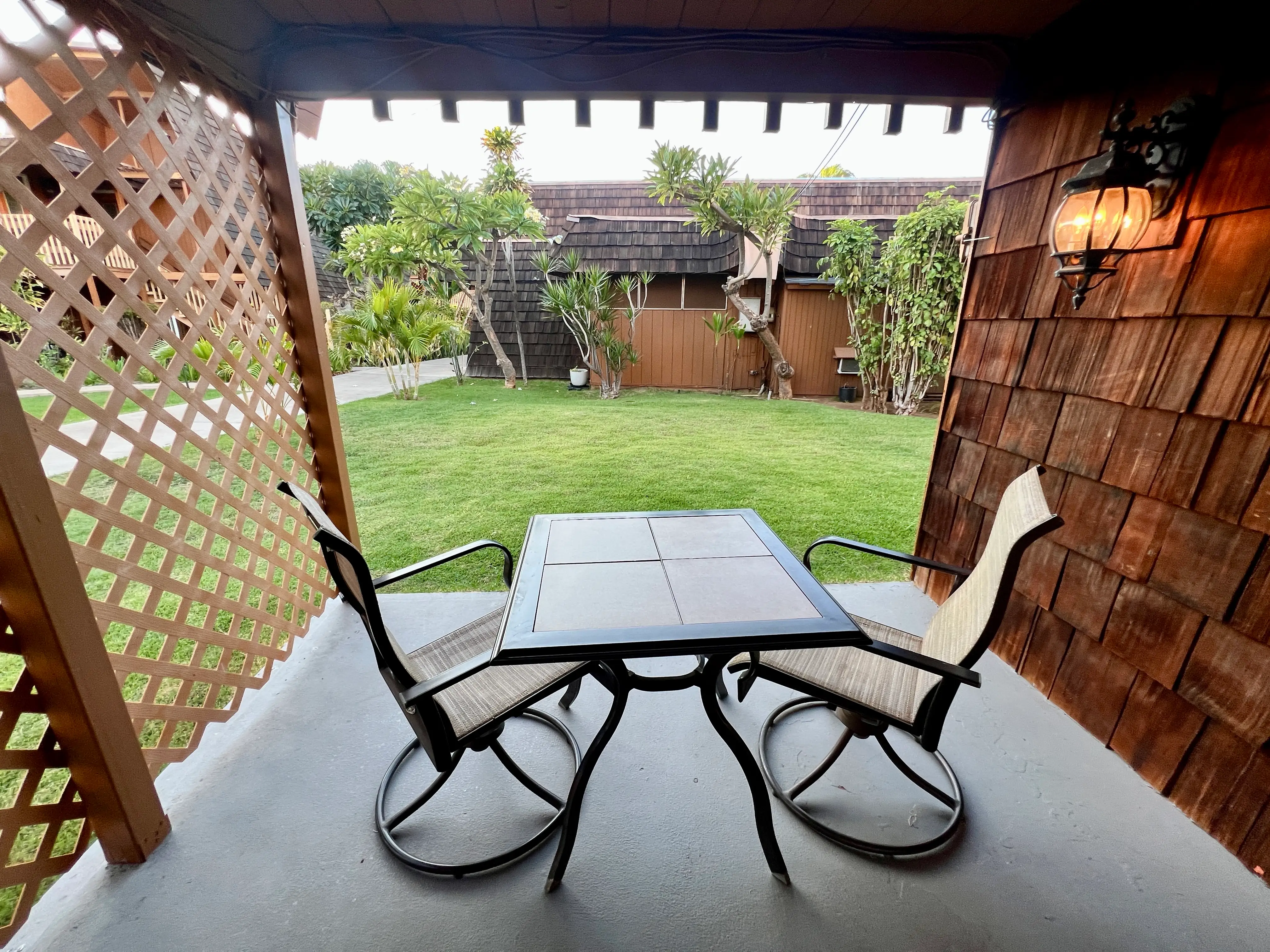 Two swiveling outdoor chairs and small table on concrete porch area in front of grass, trees