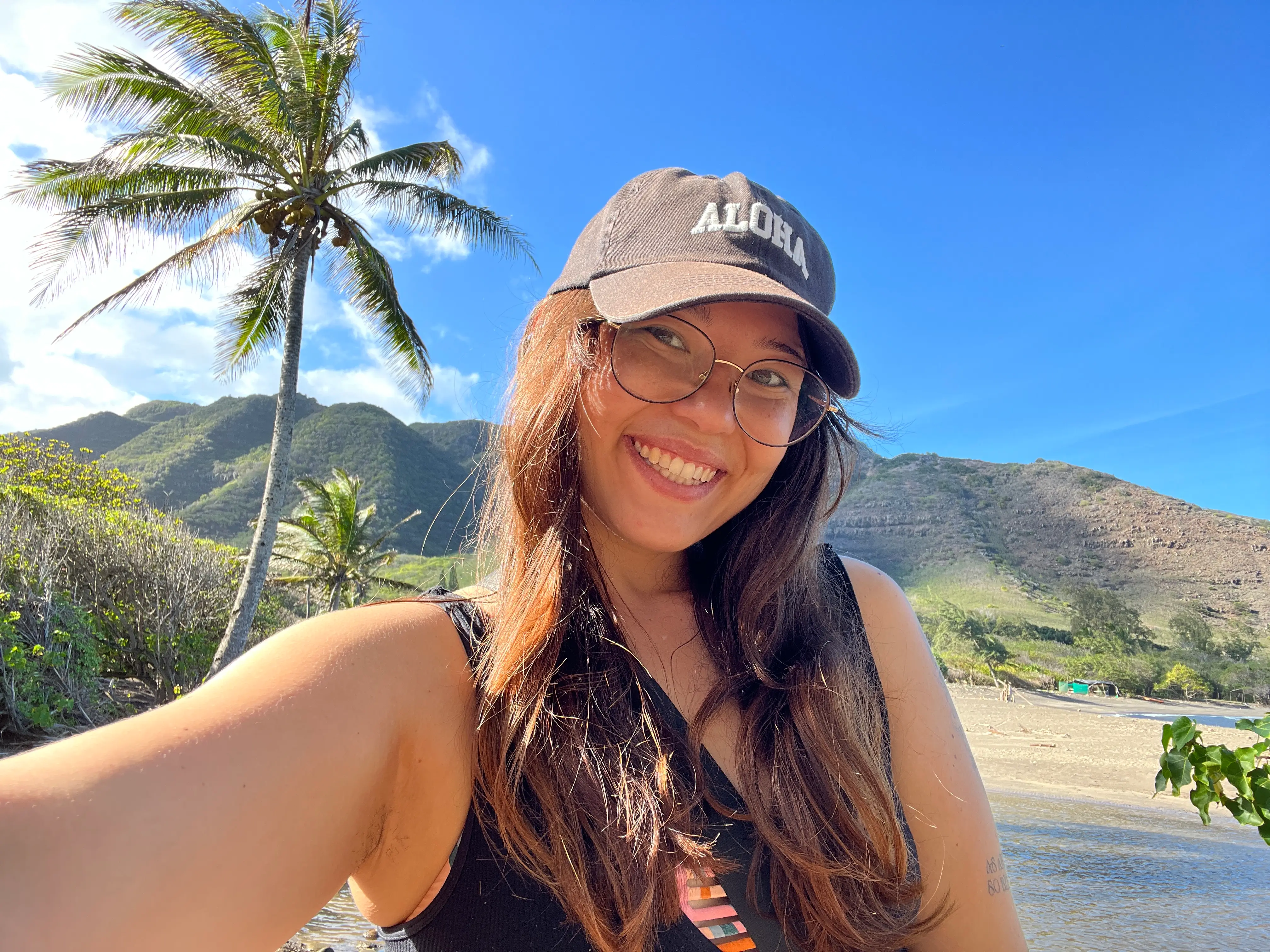 Author Ashley Probst smiling in front of palm tree wearing Aloha hat