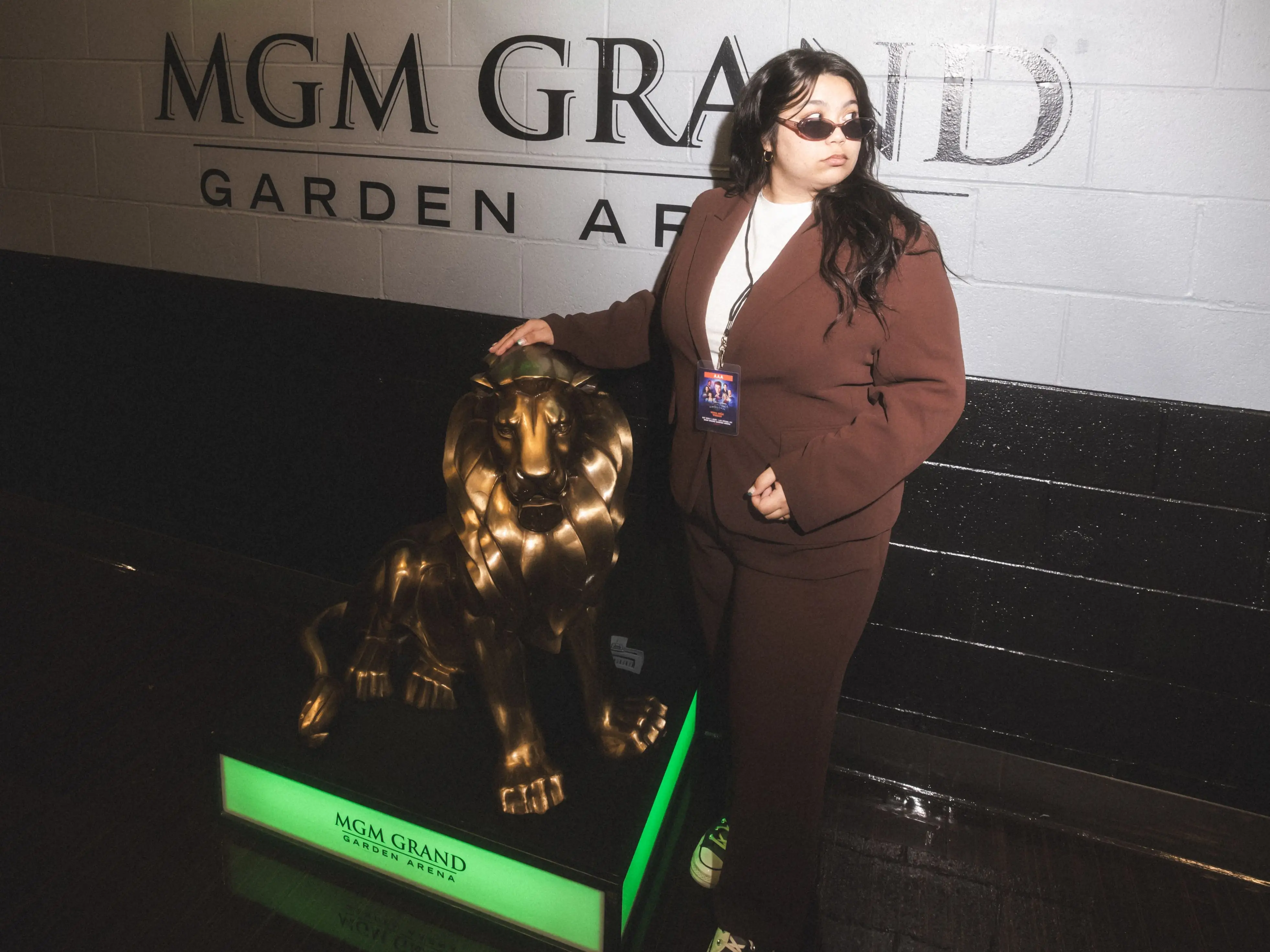Skye Smith wearing sunglasses poses beside a gold lion statue under an illuminated MGM GRAND GARDEN ARENA wall sign.