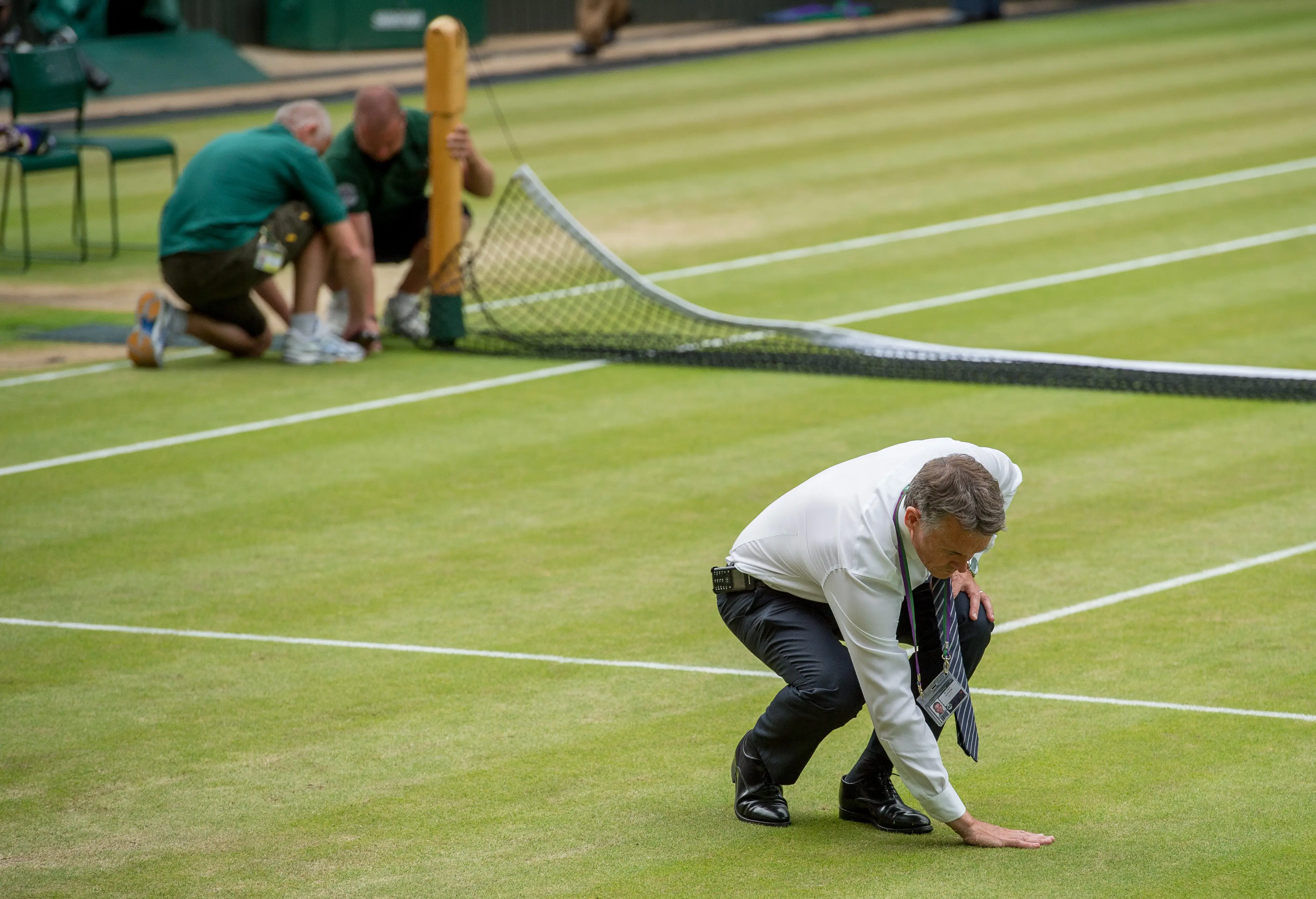 Neil Stubley, Head of Courts and Horticulture at Wimbledon, checks the grass on a court with his hand.