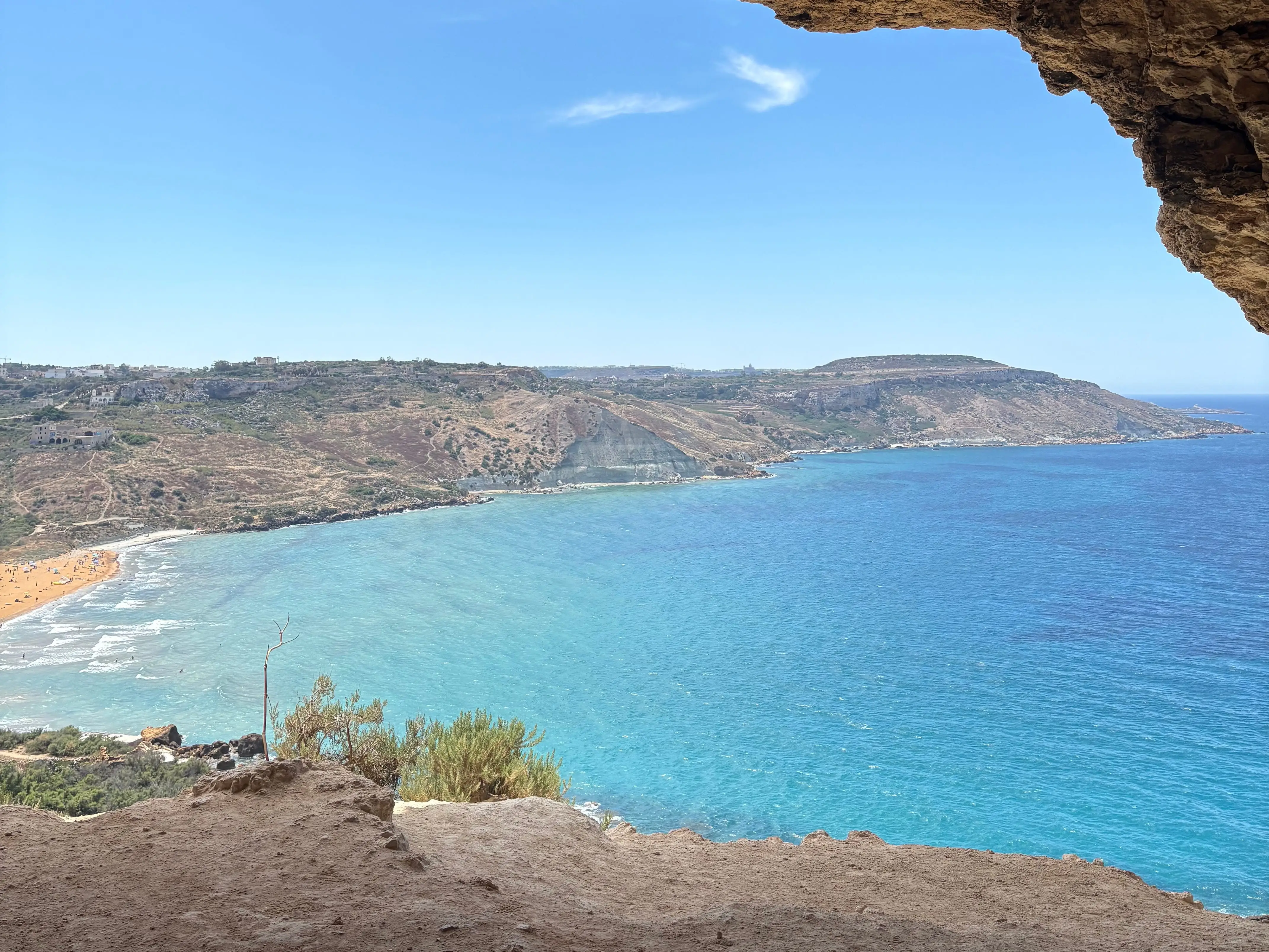 Coastal bay with turquoise water and cliffs viewed from inside a rocky cave opening in Gozo.