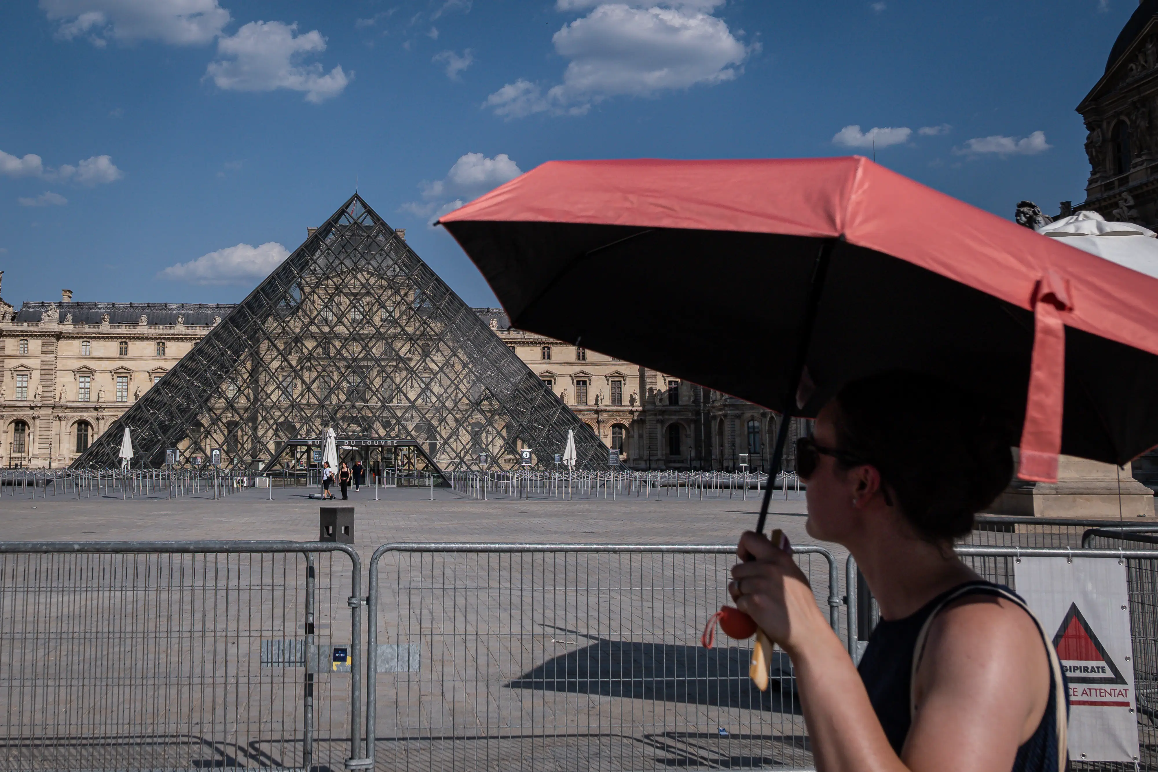 A woman uses an umbrella for shade outside the Louvre Museum during hot weather.
