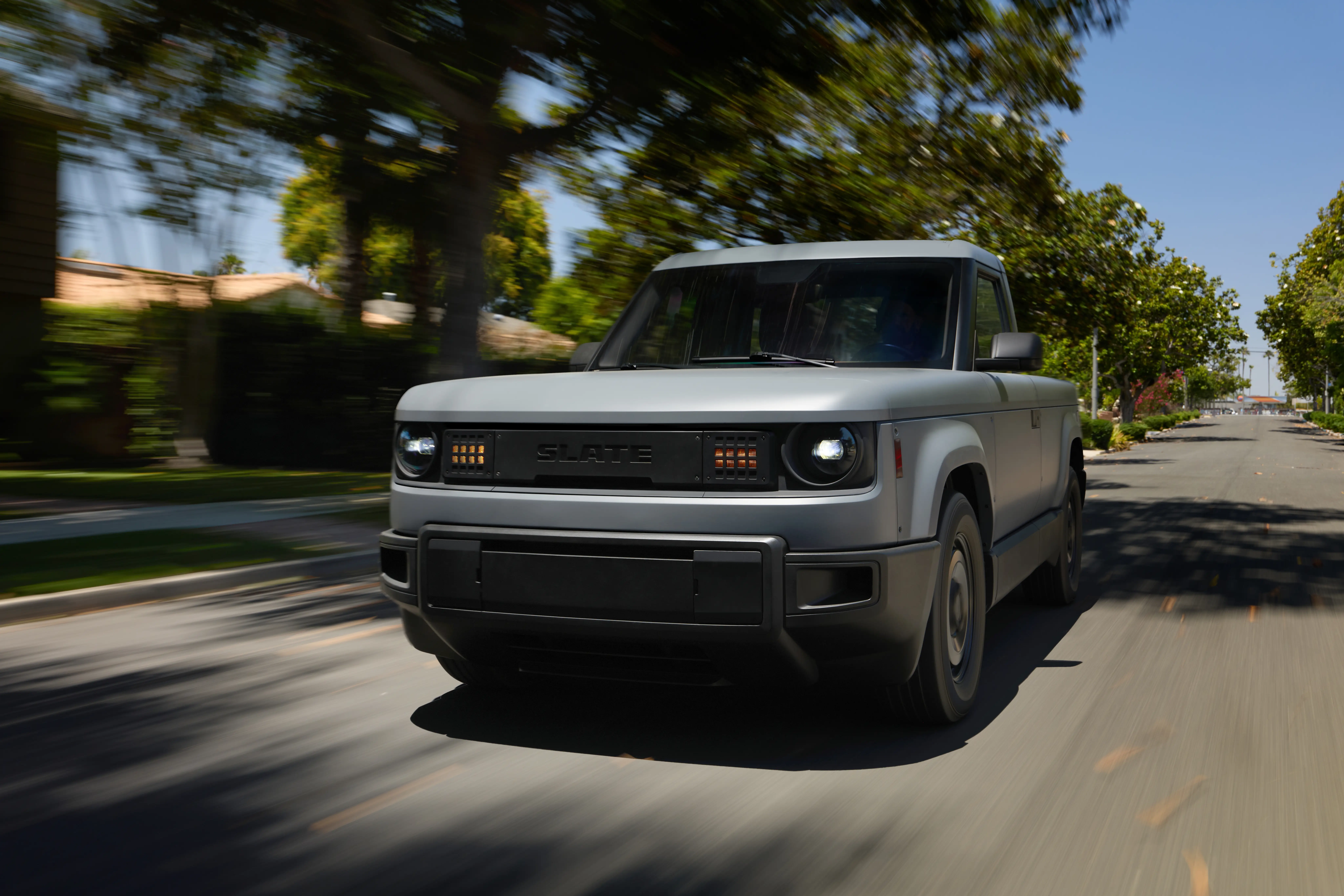 A base model Slate truck is driving down a tree-lined residential street.