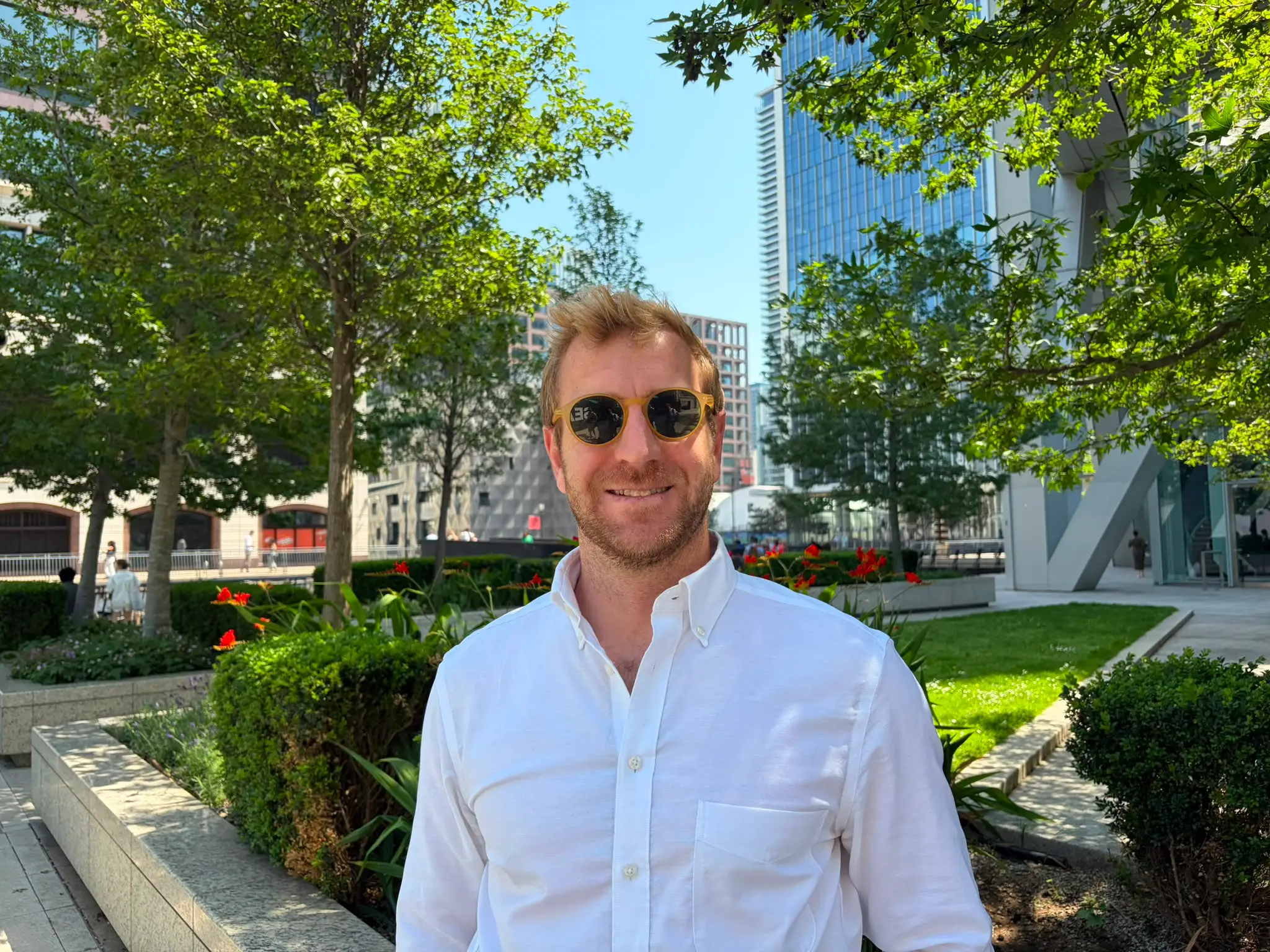 a man stands in Canary Wharf with sunglasses on