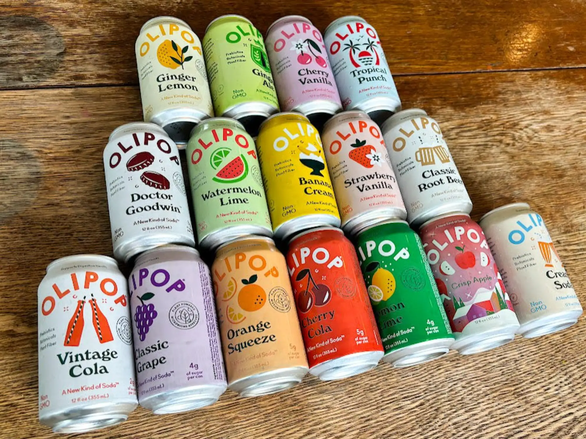 16 cans of Olipop laid out on a wooden table in a pyramid shape.
