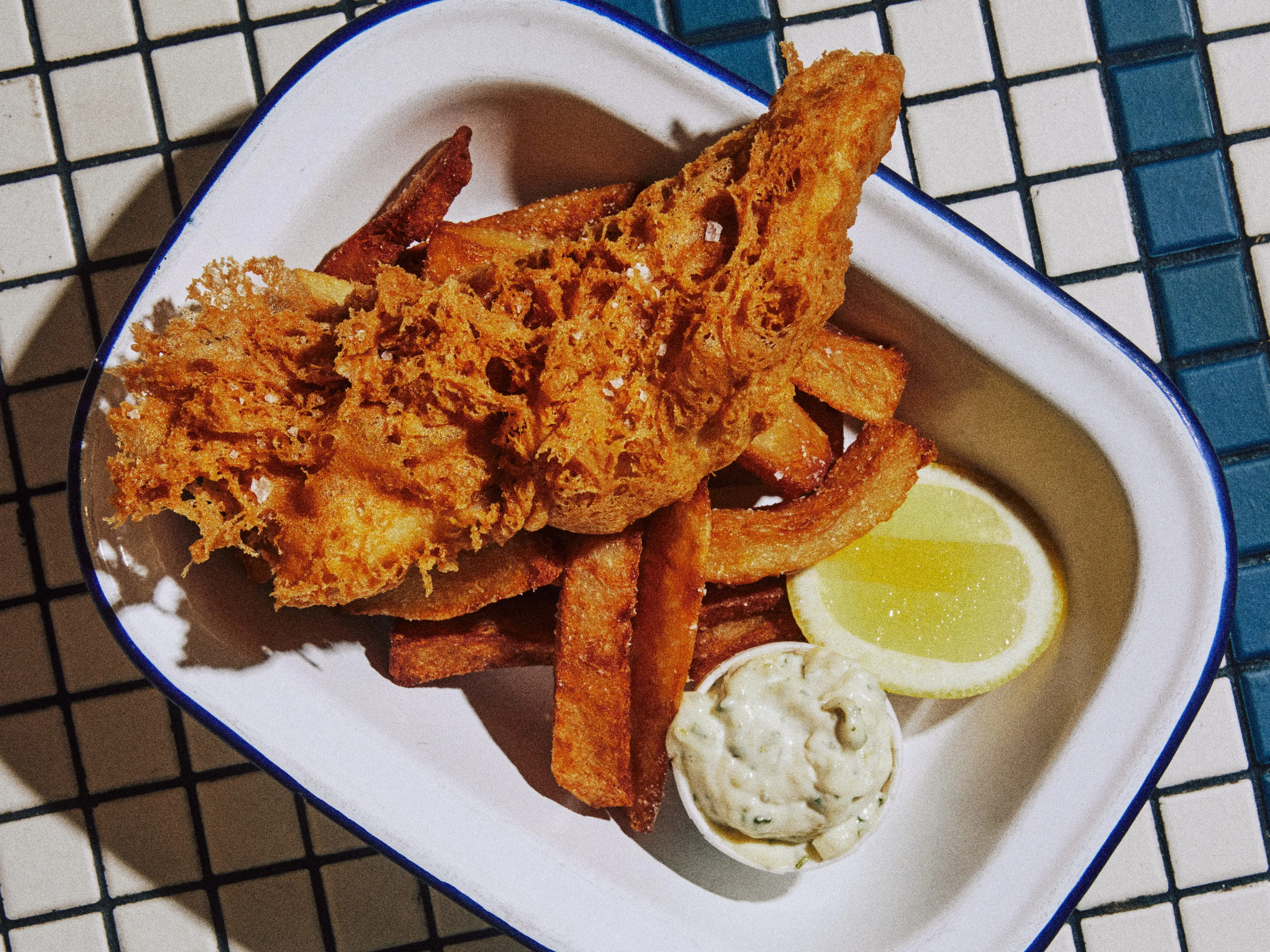 Fish and chips, a lemon wedge, and tartar sauce on a white tray at Dame.