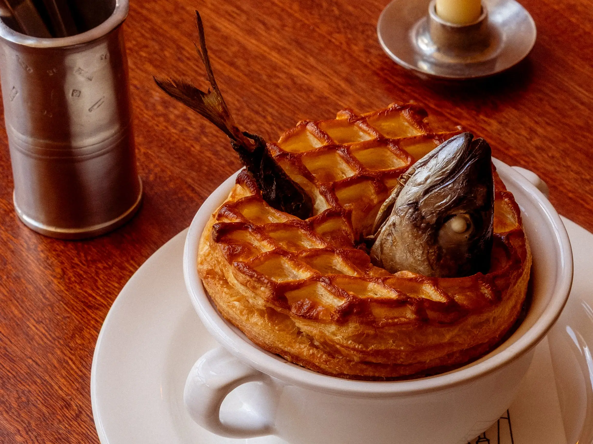 A fish pie with a lattice crust and a fish head sits in a white cup on a wooden table at Dean's.