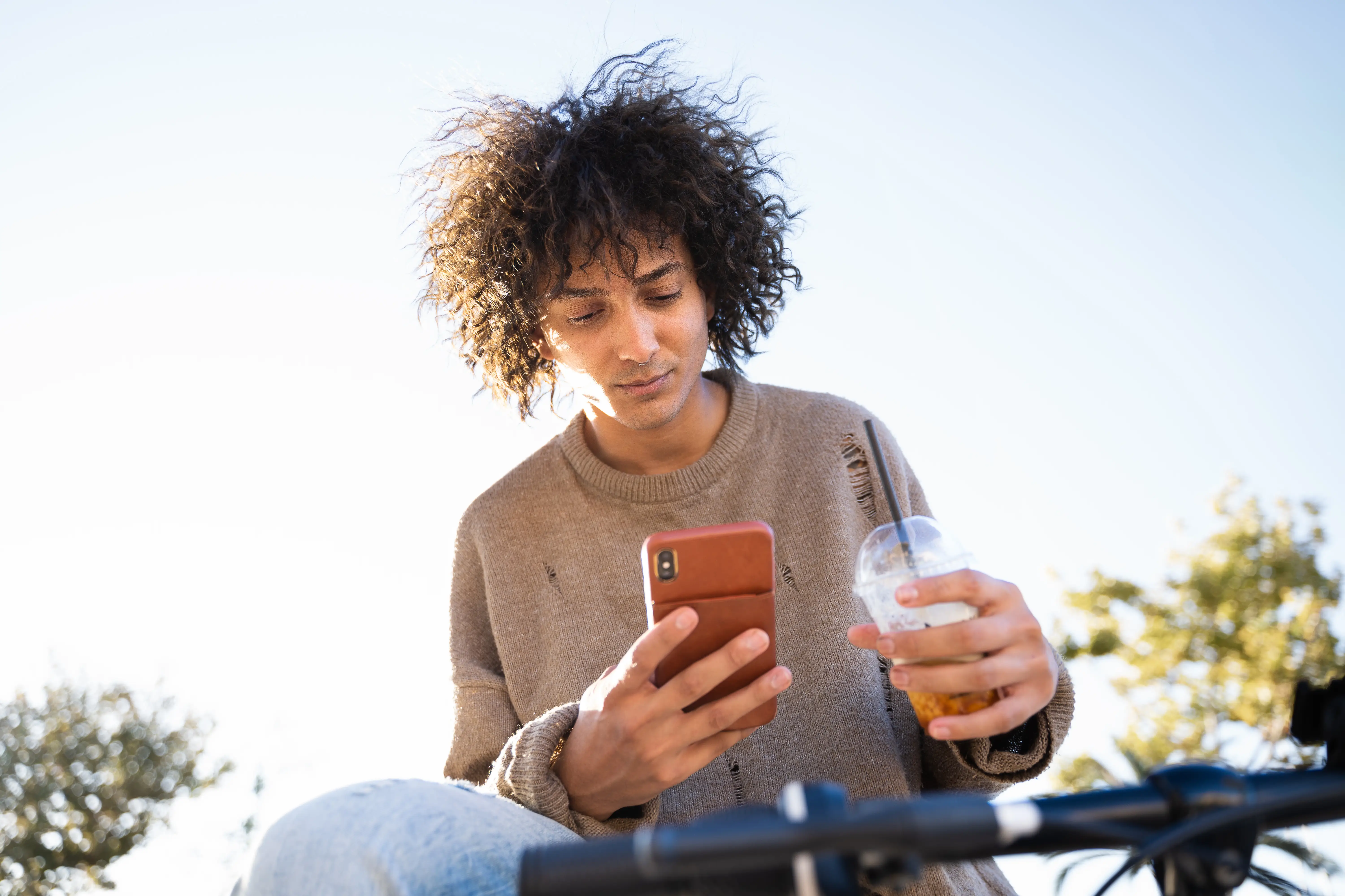 A man drinks an iced coffee while looking at his phone.