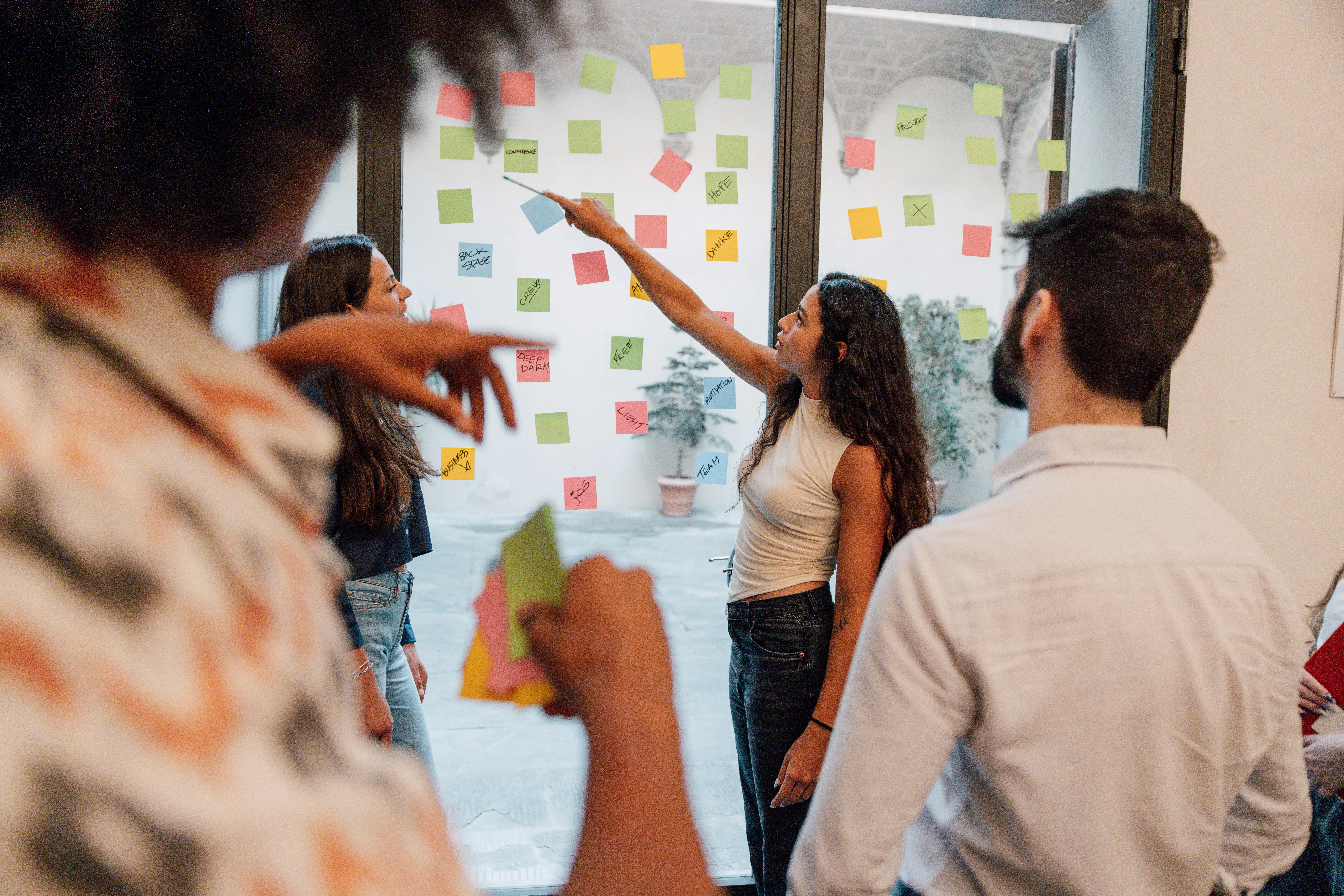 a group of gen z coworkers in an office conference room looking at post its on the window
