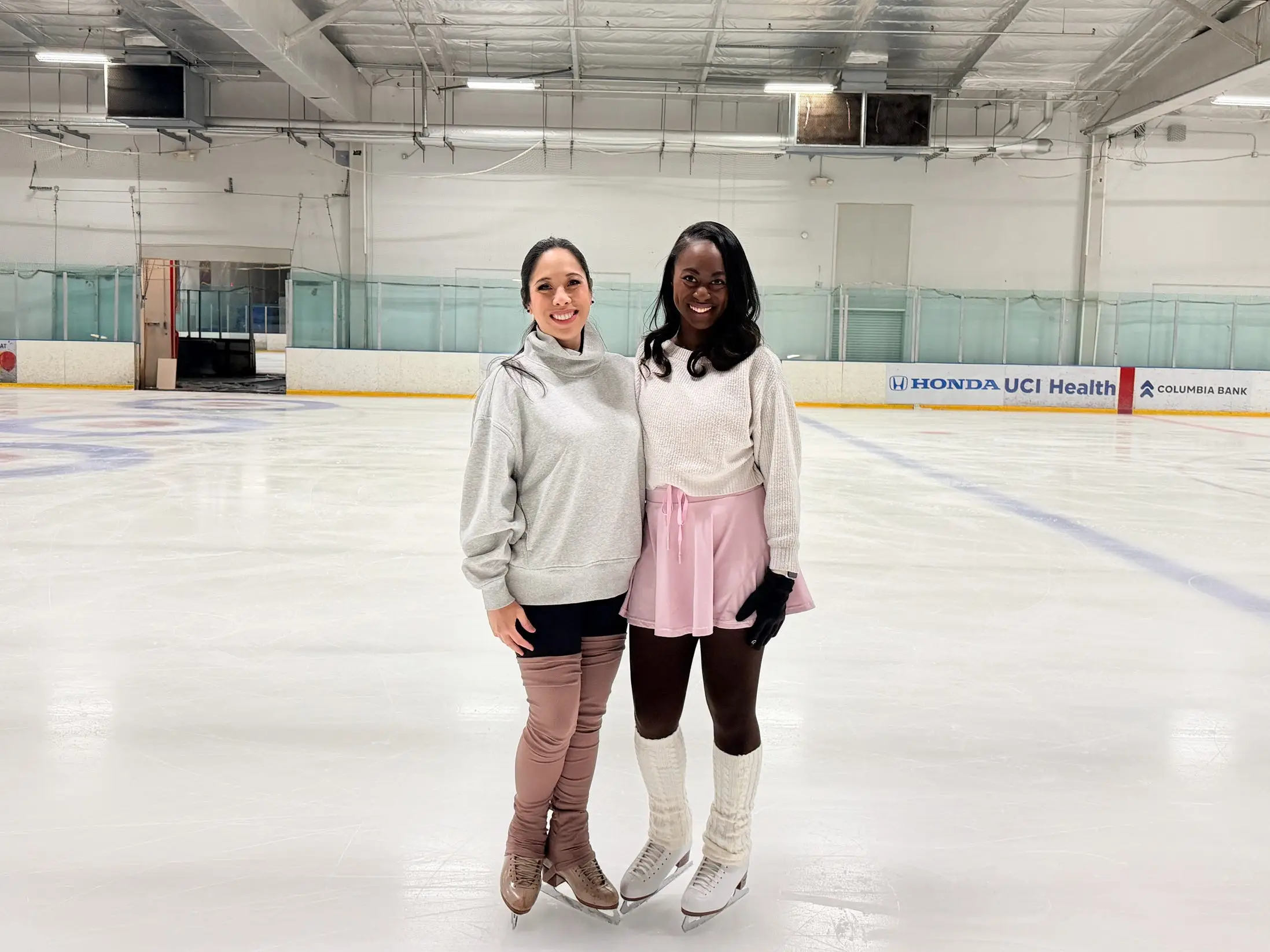 The writer posing next to her ice skating coach on an indoor ice rink.