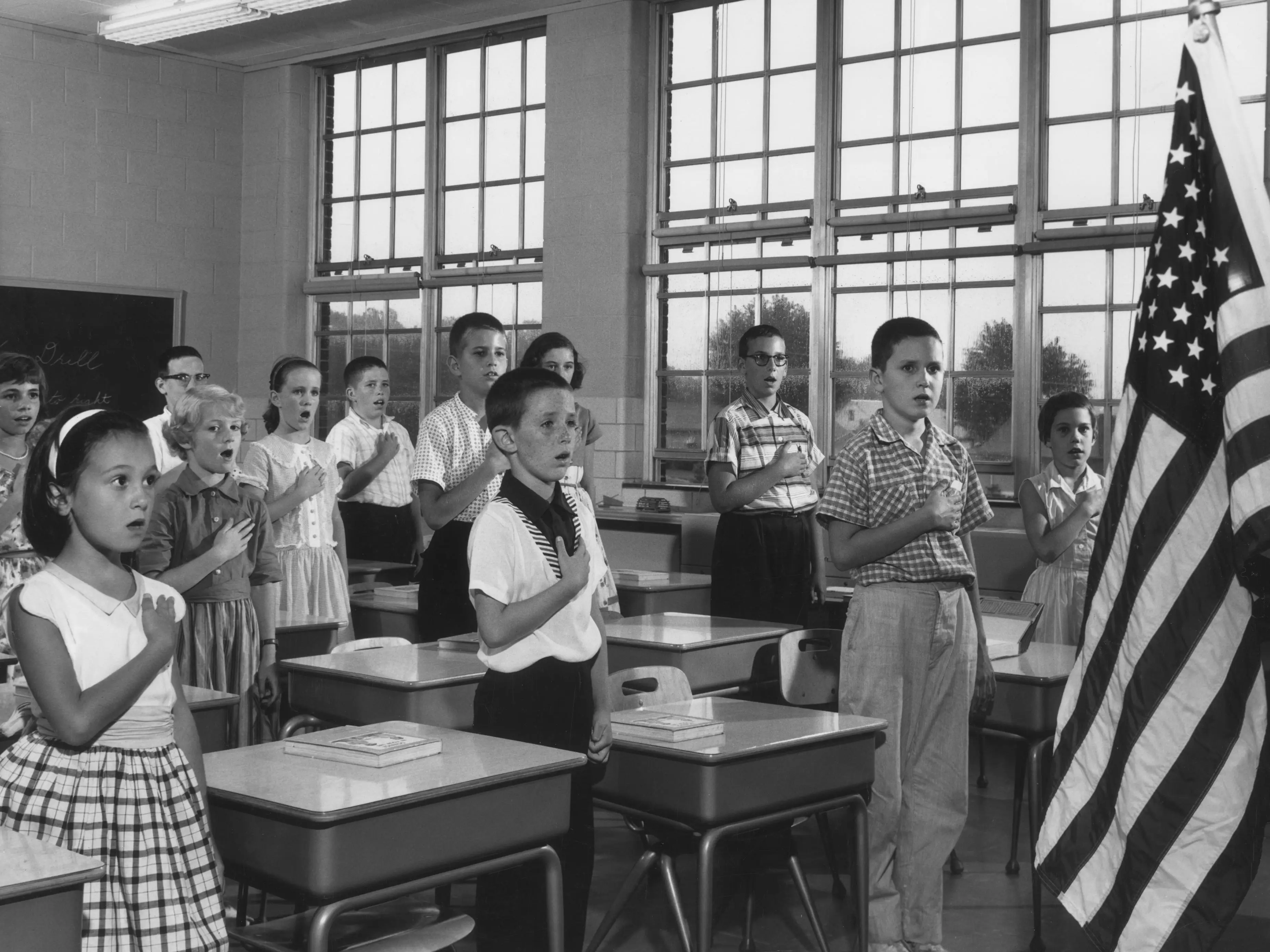 Historical photo of children reciting the pledge of allegiance in a classroom.