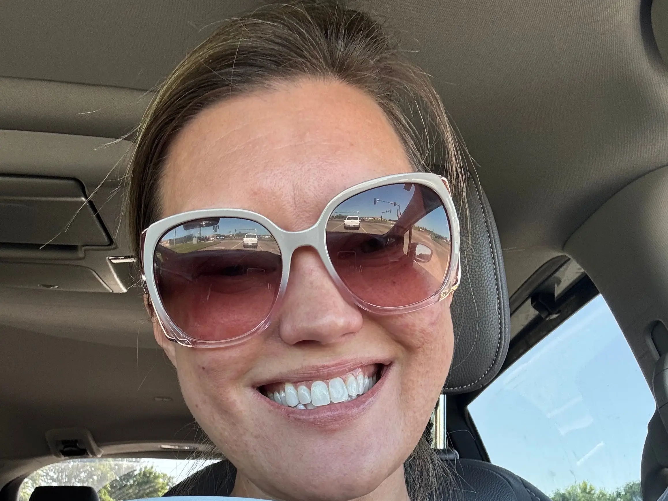 The author is taking a selfie in a car, wearing sunglasses and holding a mug.