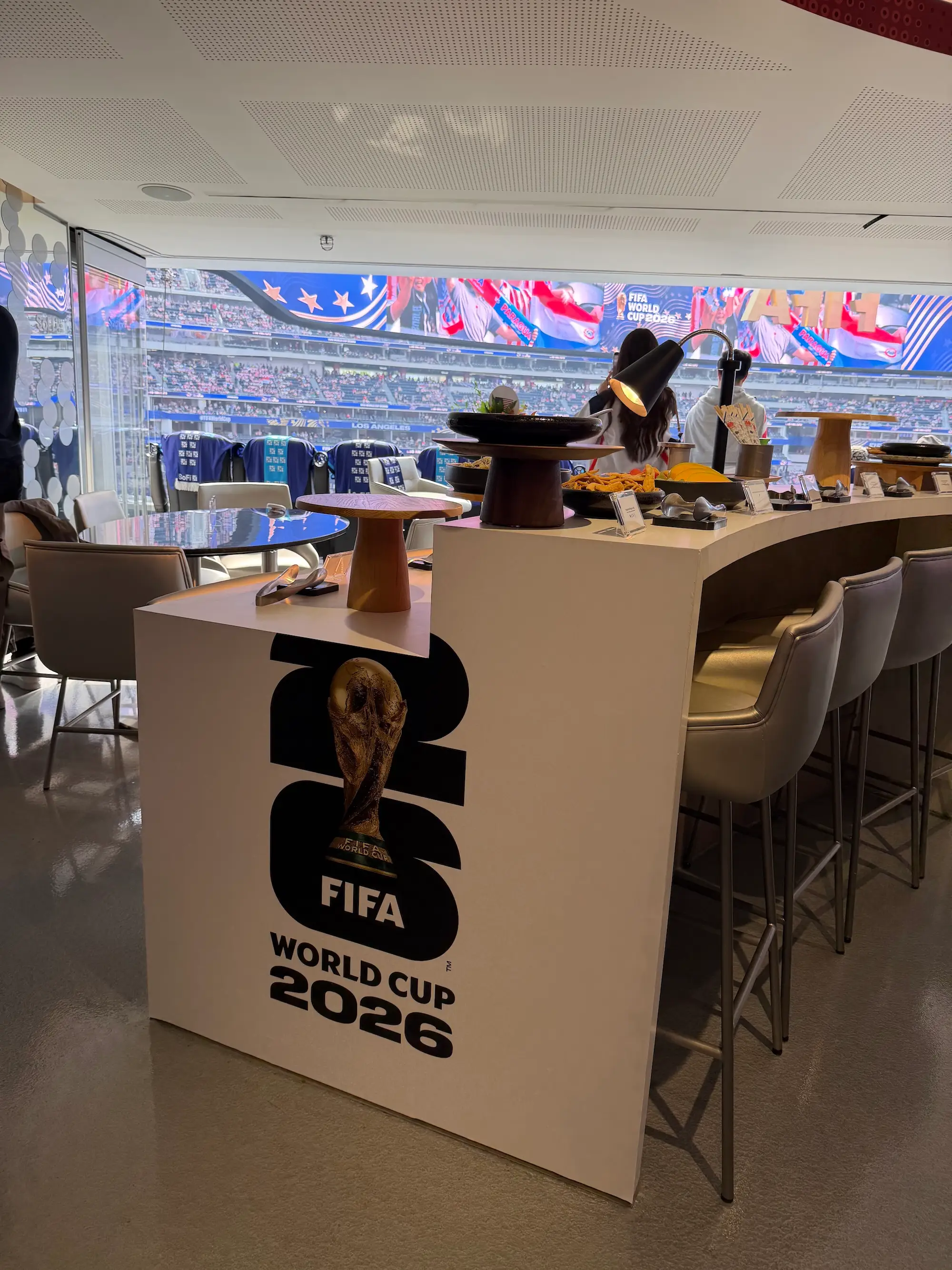 FIFA World Cup 2026 branded hospitality display inside a stadium suite overlooking seating and digital banners.