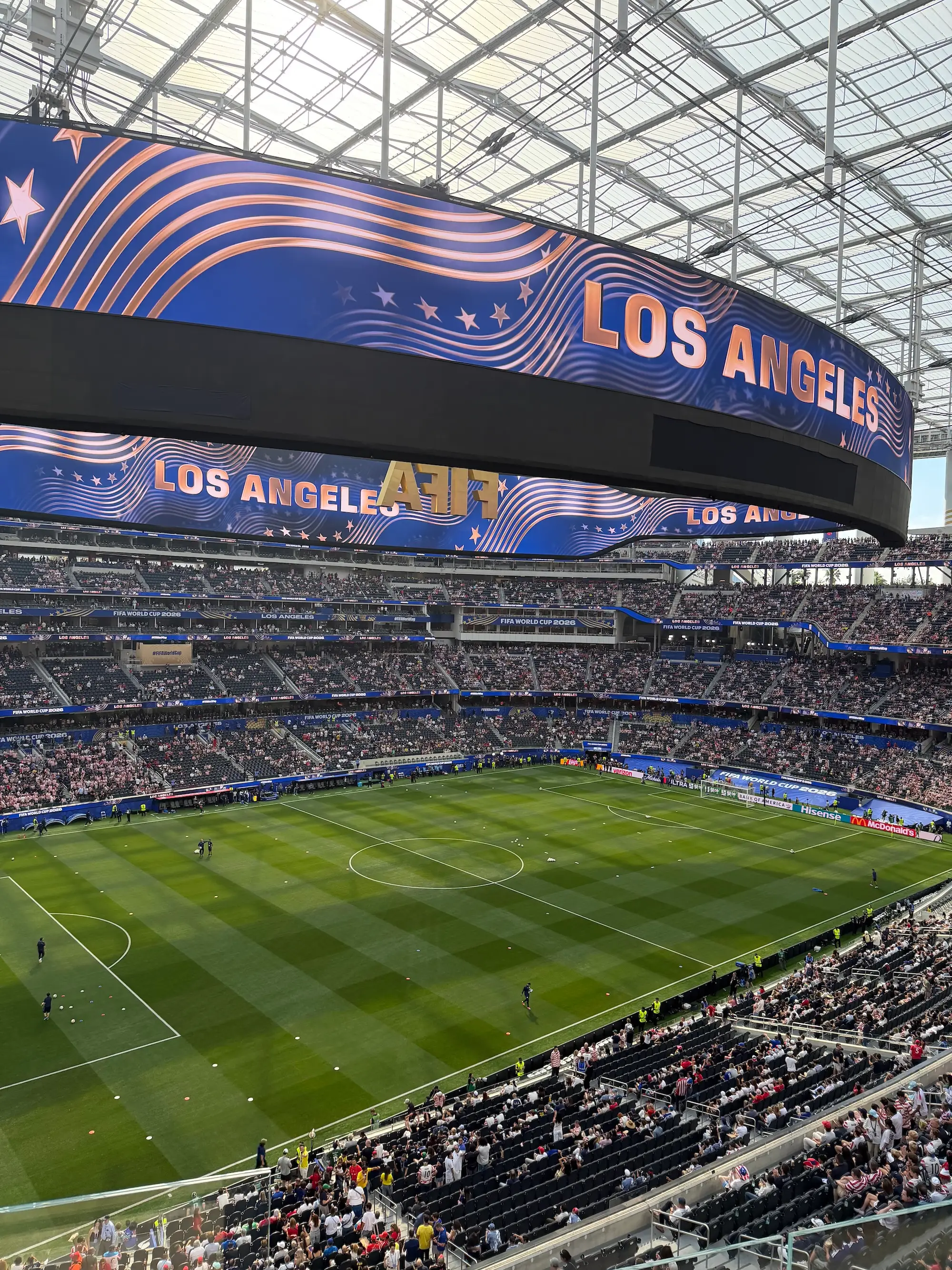 Crowd-filled SoFi Stadium displays Los Angeles graphics above a soccer pitch.
