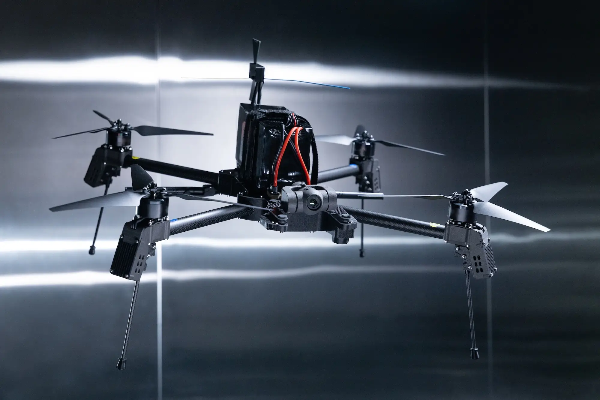 Quadcopter drone with a front camera is shown against a dark metallic background.