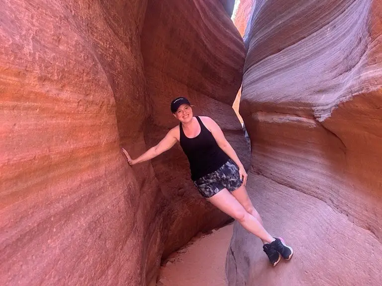 Woman leaning between narrow red rocks, smiling