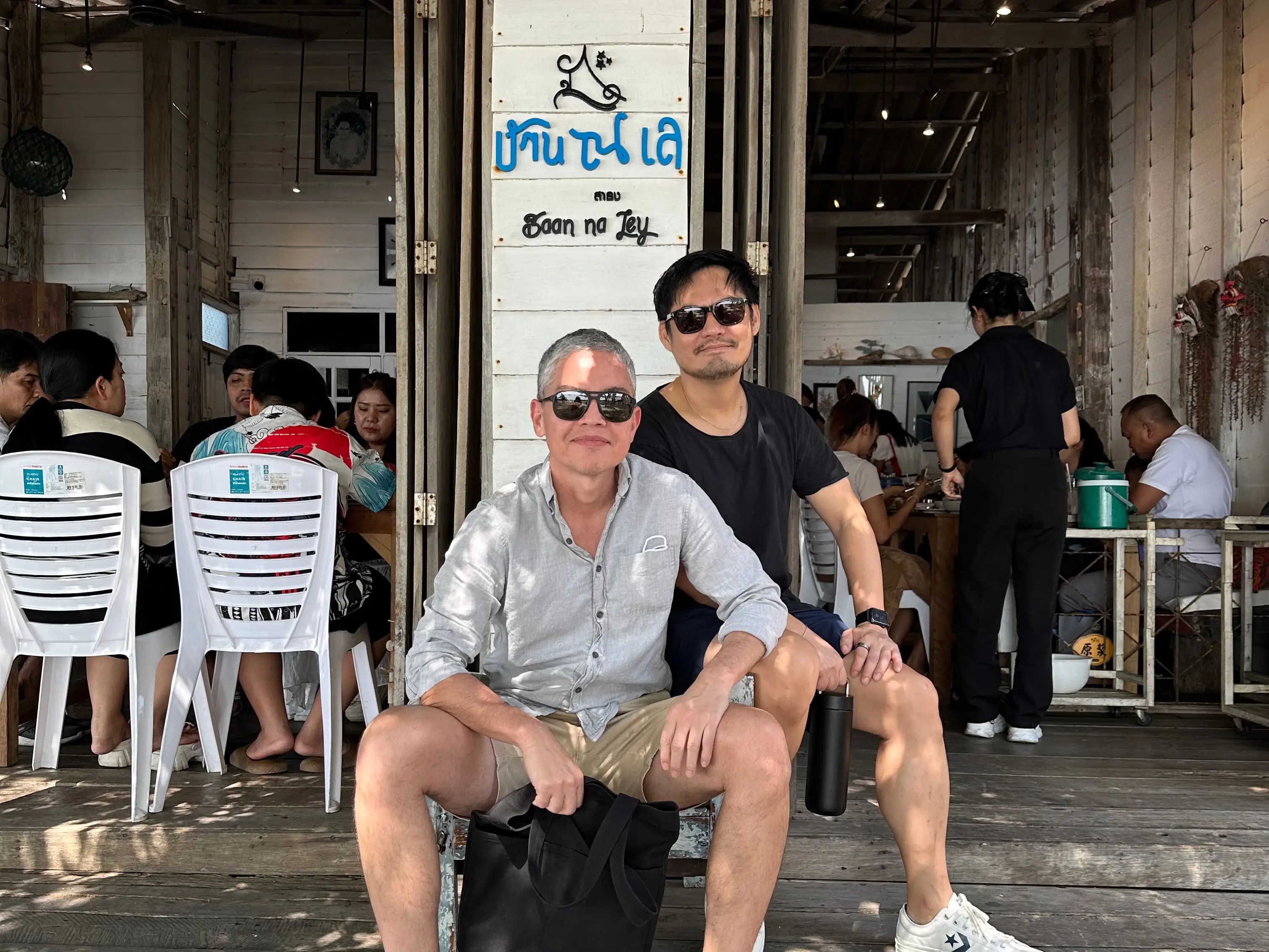 Two men are seated outside an open-air restaurant in Bangkok.