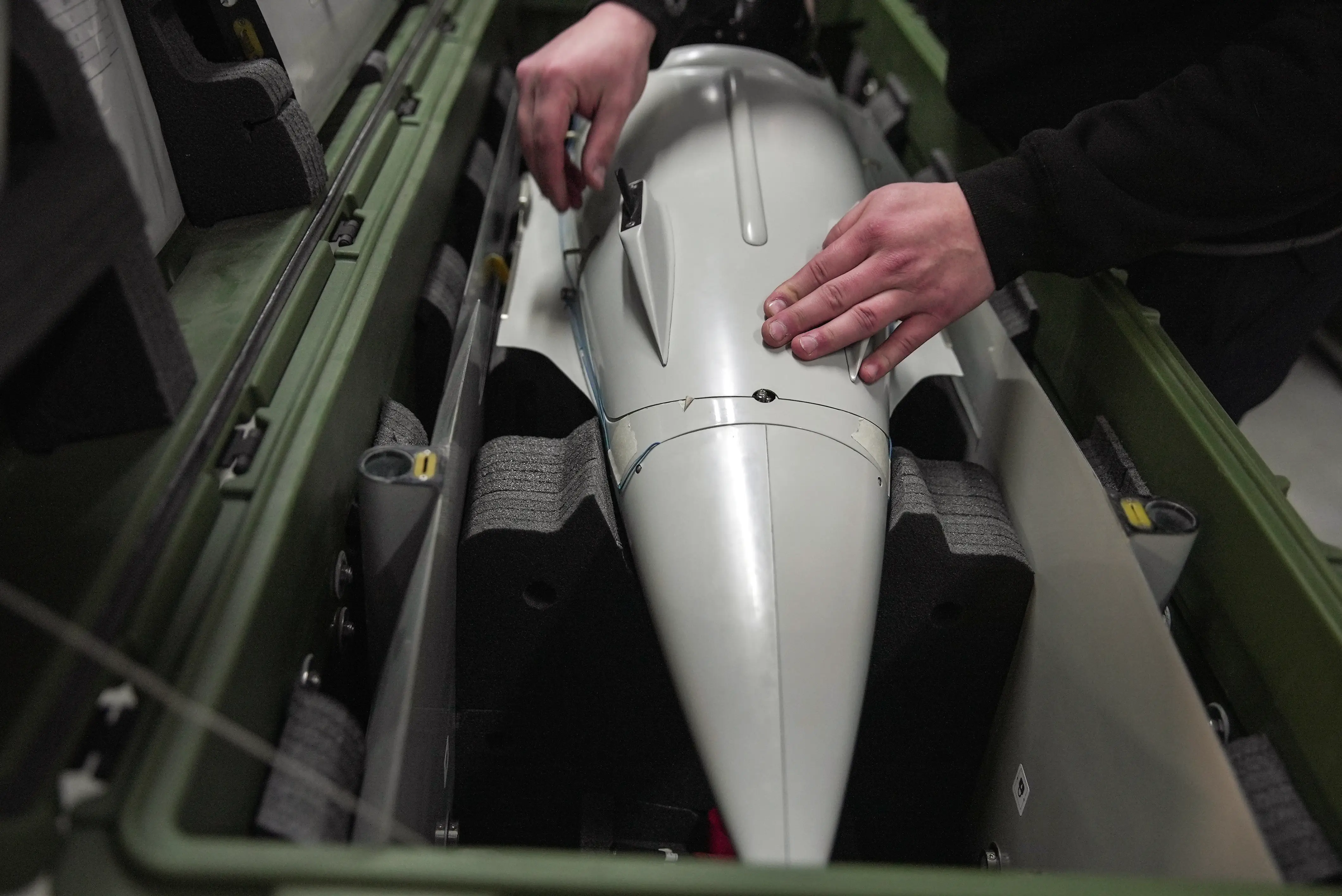 A large white drone part in a khaki box with hands touching it