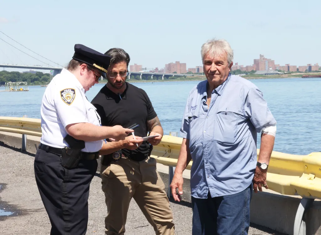 Giuseppe Oppedisano with a bandaged arm, after being rescued from a plane crash, standing next to a police officer and another man by the East River.