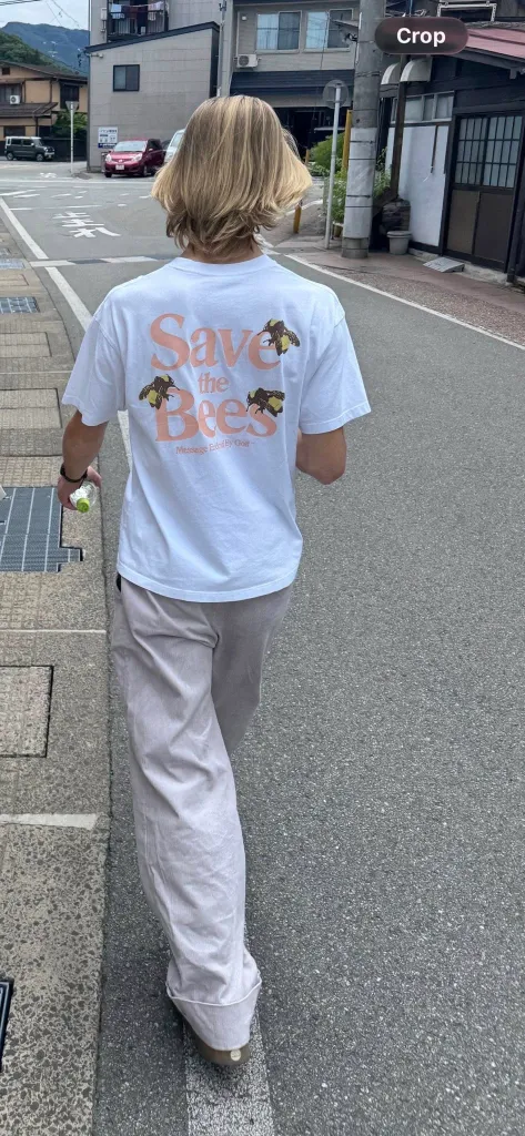 A person with blond hair walks away from the camera, wearing a white t-shirt that says 
