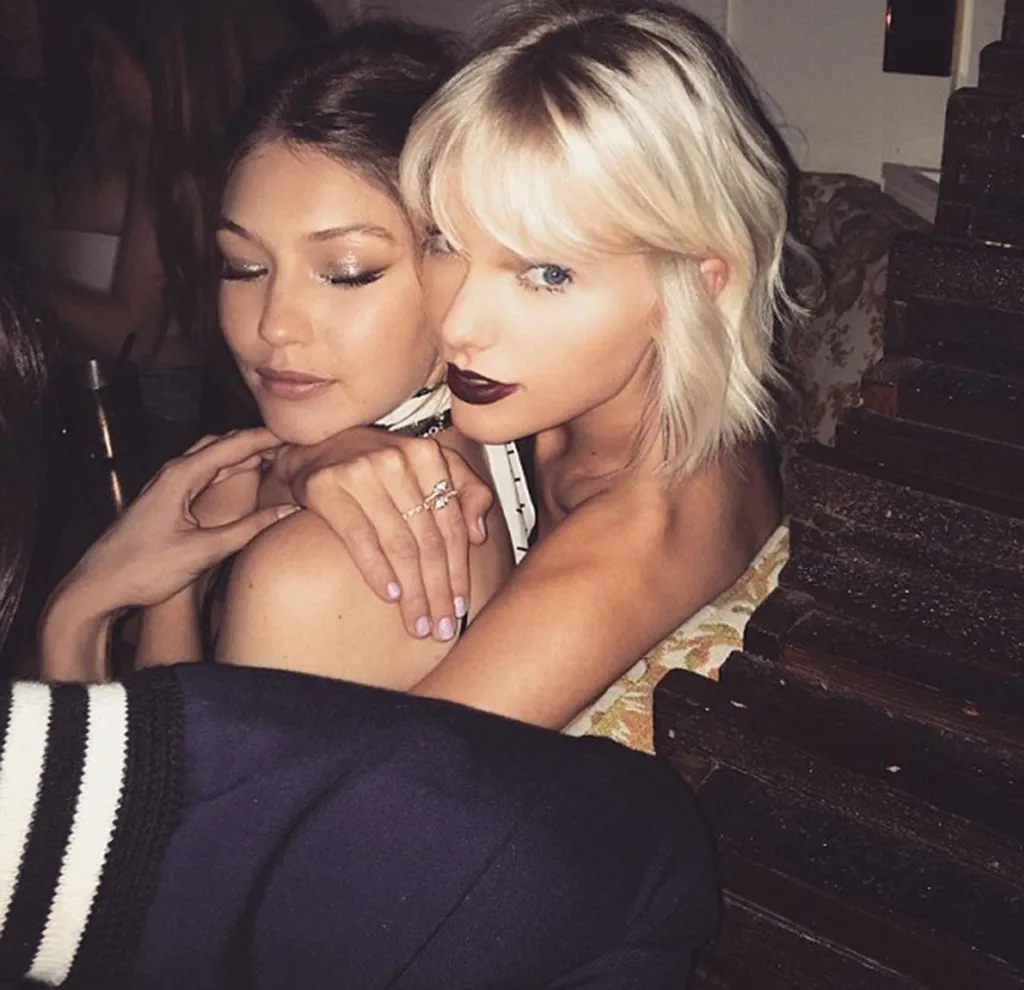 Taylor Swift with blonde hair and dark lipstick embracing Gigi Hadid.