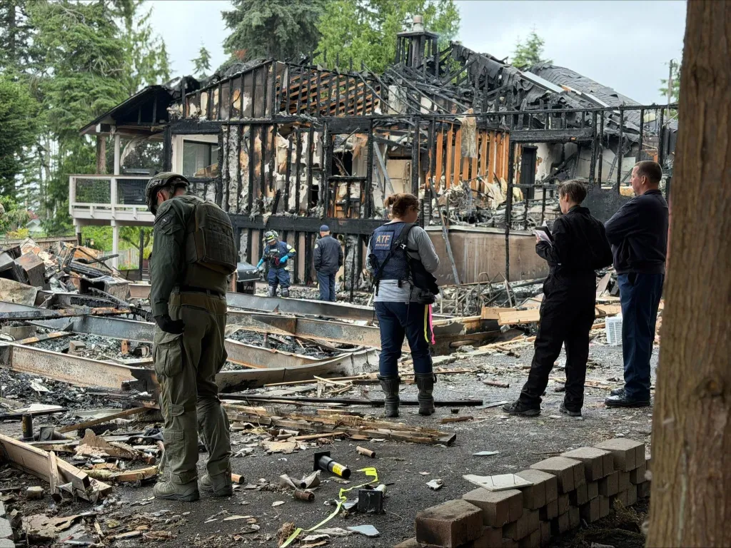 Law enforcement and officials examine the burnt-out shell of a house.