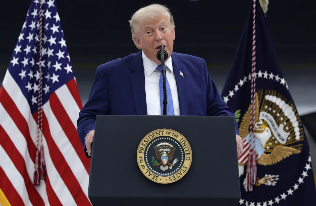 President Donald Trump speaks at a podium with the Seal of the President of the United States, flanked by the American flag and a flag with the presidential seal.