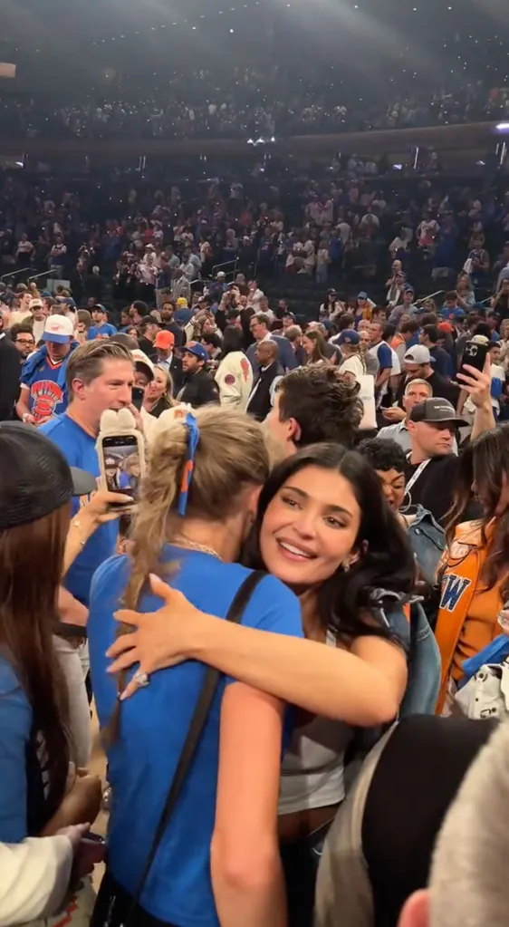 Kylie Jenner hugging a person in a blue shirt at a crowded sporting event.