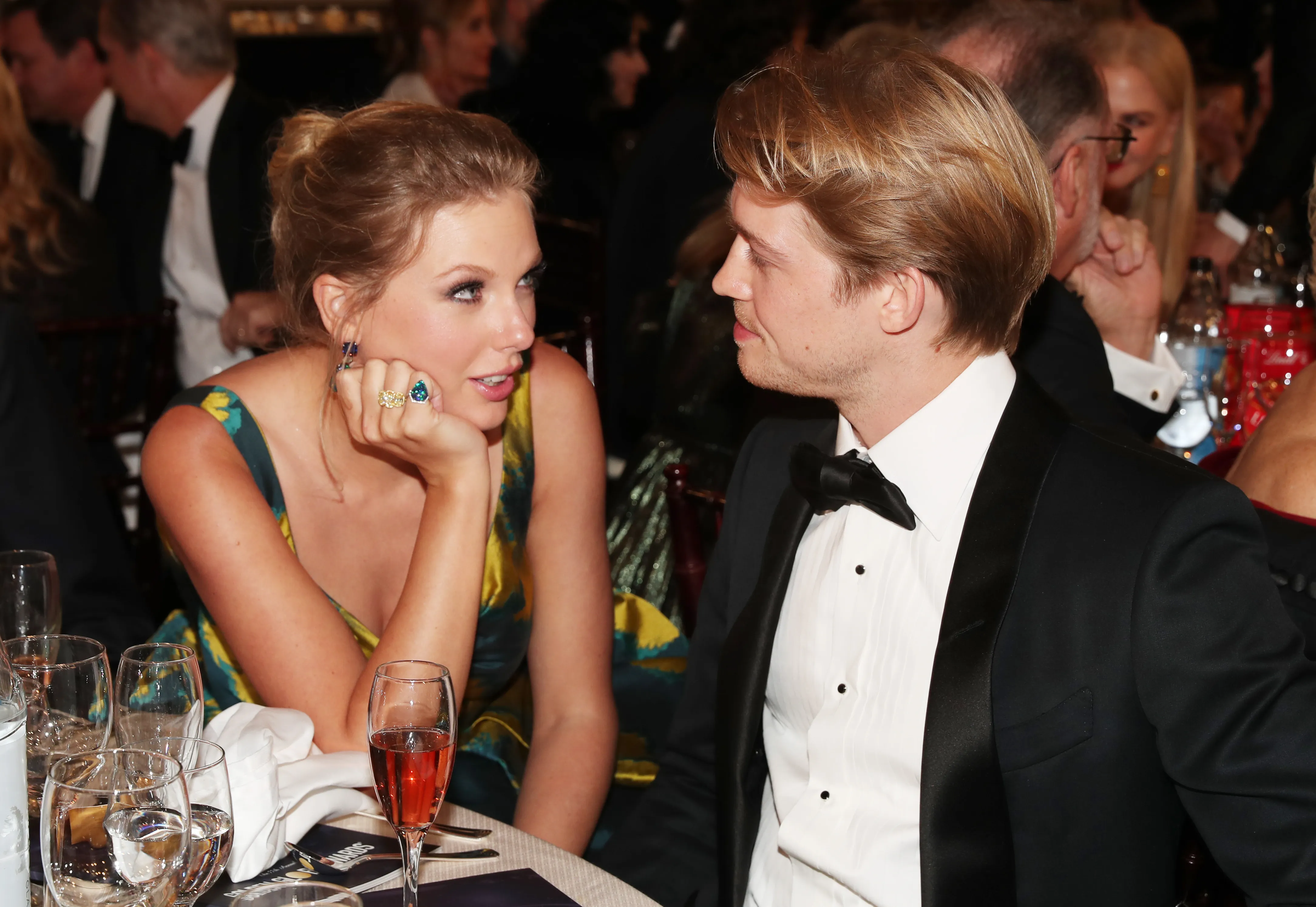 Taylor Swift and Joe Alwyn seated at a table, looking at each other and talking.