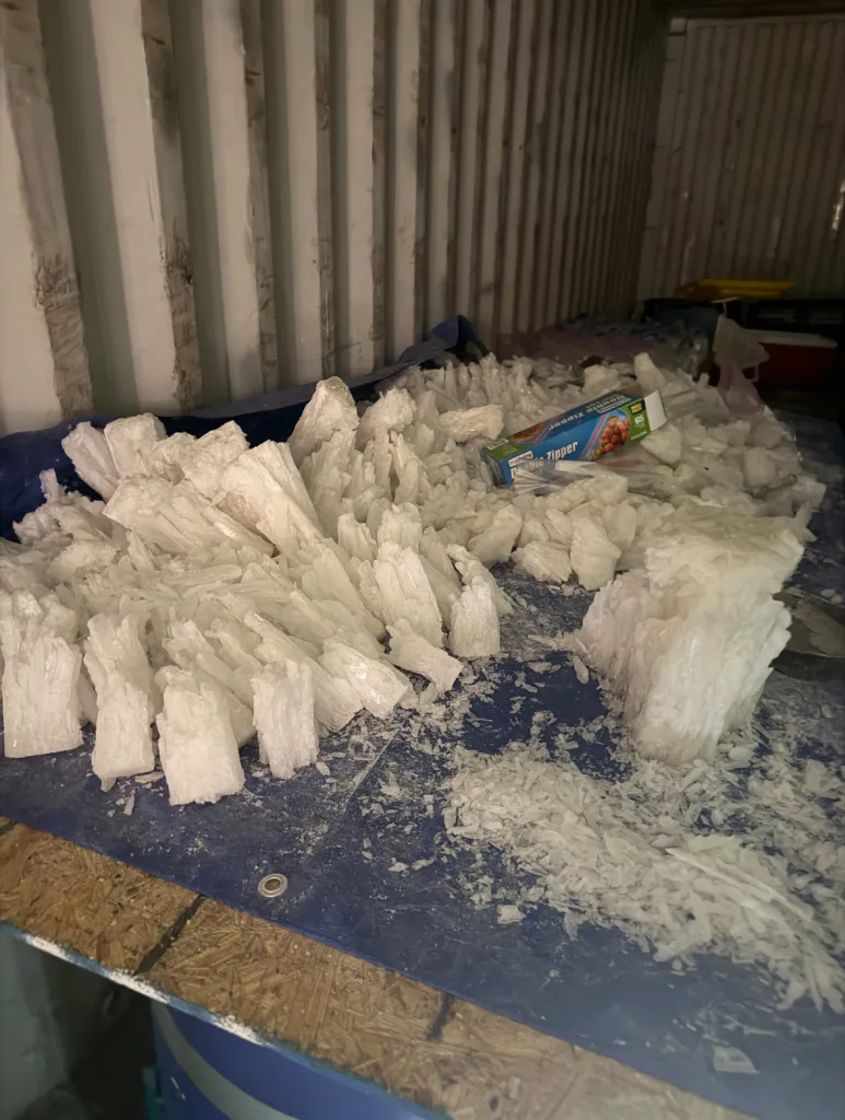 Large quantities of methamphetamine crystals and a box of plastic zipper bags, found in a cargo container, indicating a narcotics production operation.