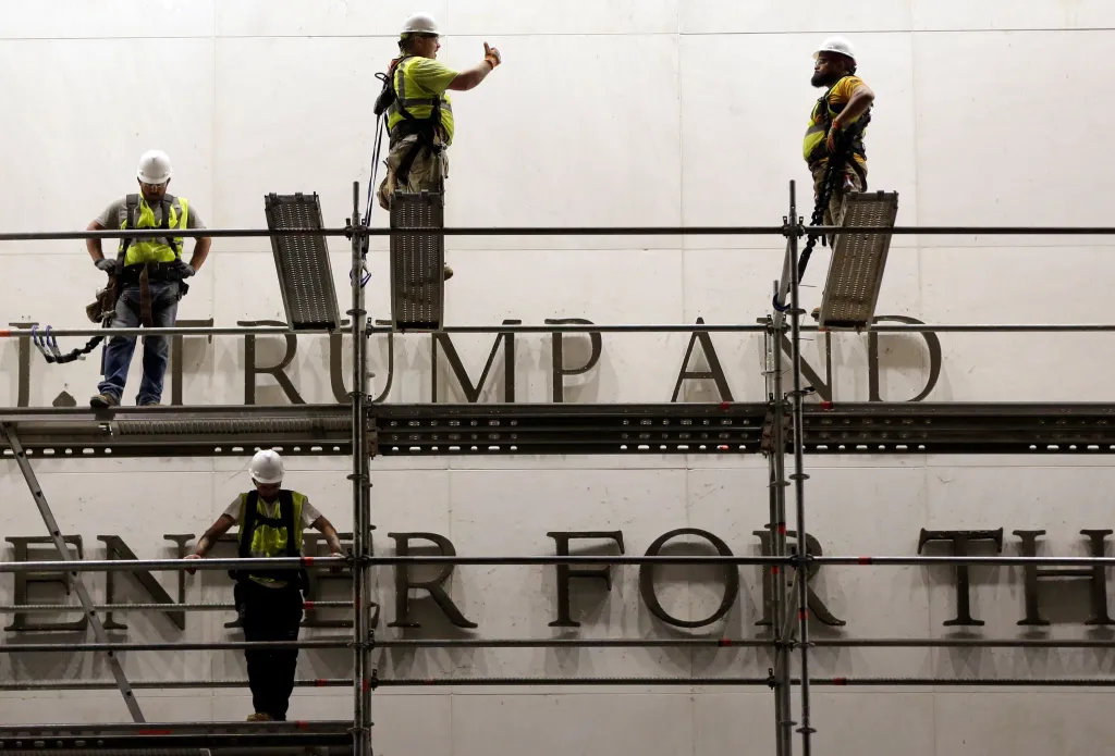 Construction workers on scaffolding in front of a white building with the letters 