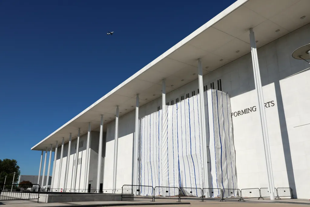 Workers assemble scaffolding on the side of the John F. Kennedy Center for the Performing Arts, while people watch.