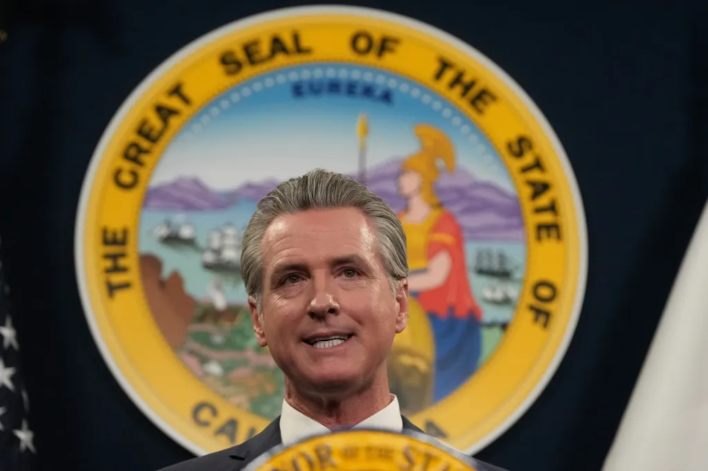 California Governor Gavin Newsom speaking in front of the Great Seal of the State of California.