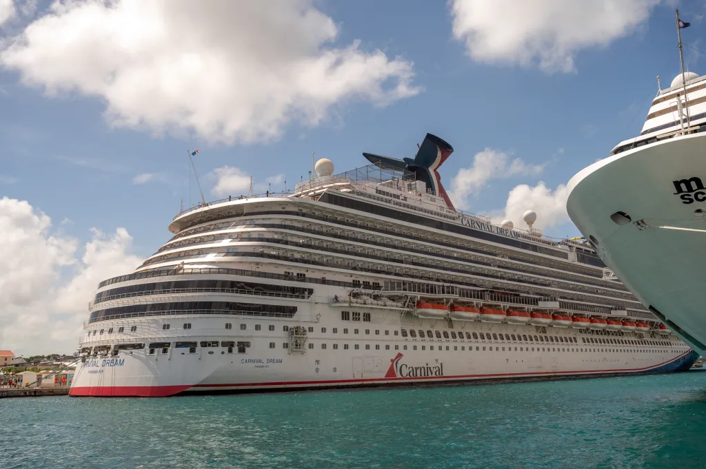 Side view of the Carnival Dream cruise ship docked in the Bahamas, with green water and a blue sunny sky.