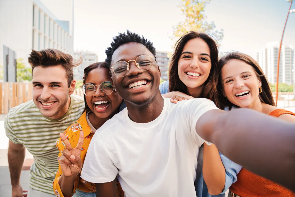 Group of five smiling, diverse young friends taking a selfie outdoors.