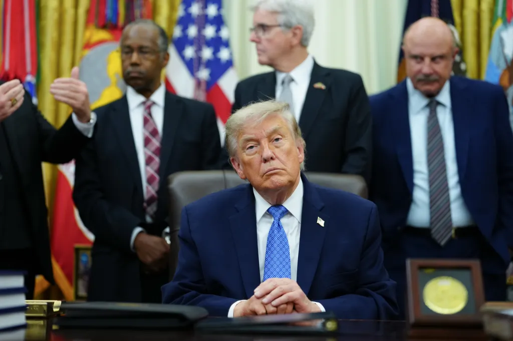 Donald Trump sitting at a desk, surrounded by men including Ben Carson and Dr. Phil, during the Faith and Freedom Coalition's 2026 Road to Majority Policy Conference.