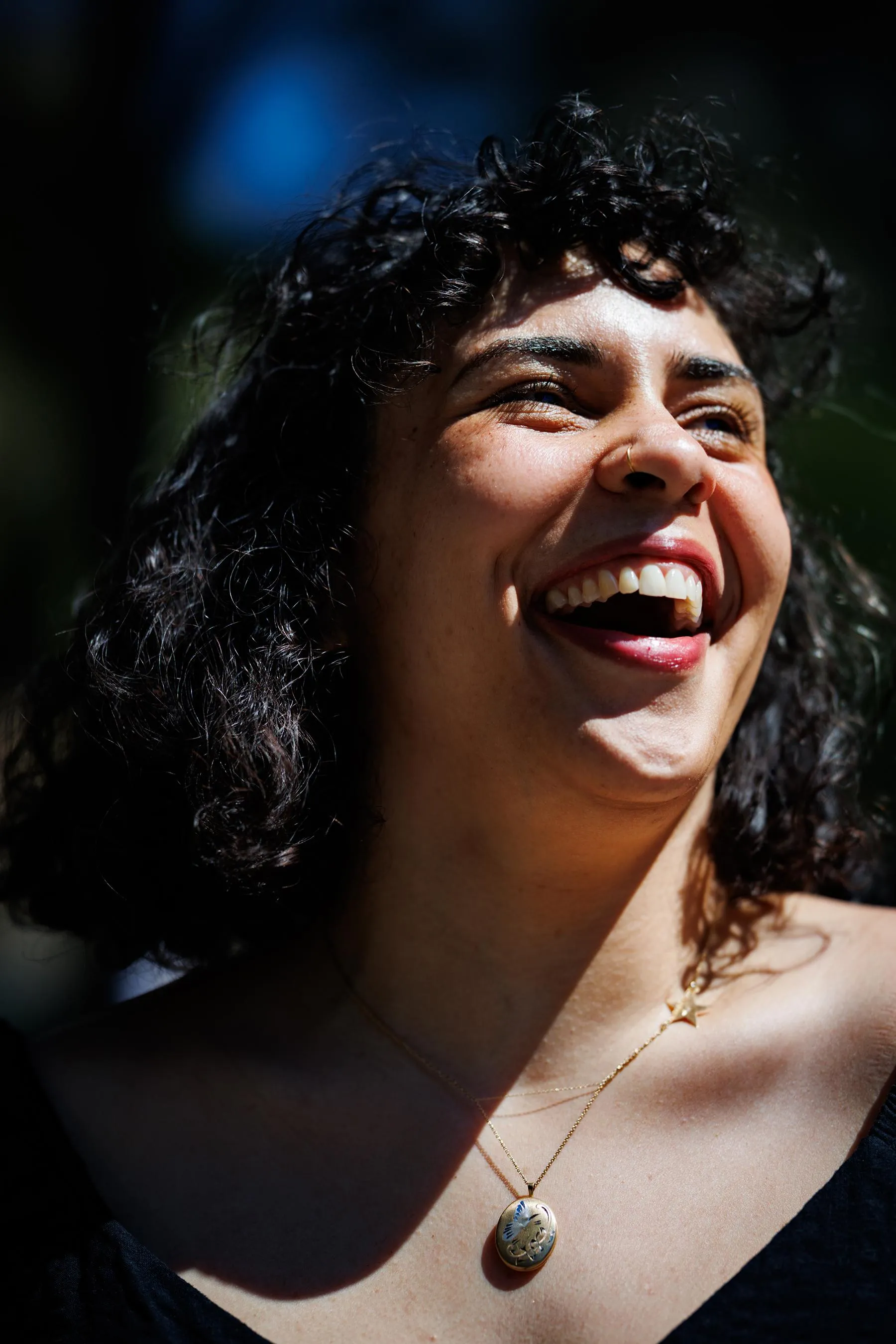 a woman is outside, laughing while squinting in the sunlight