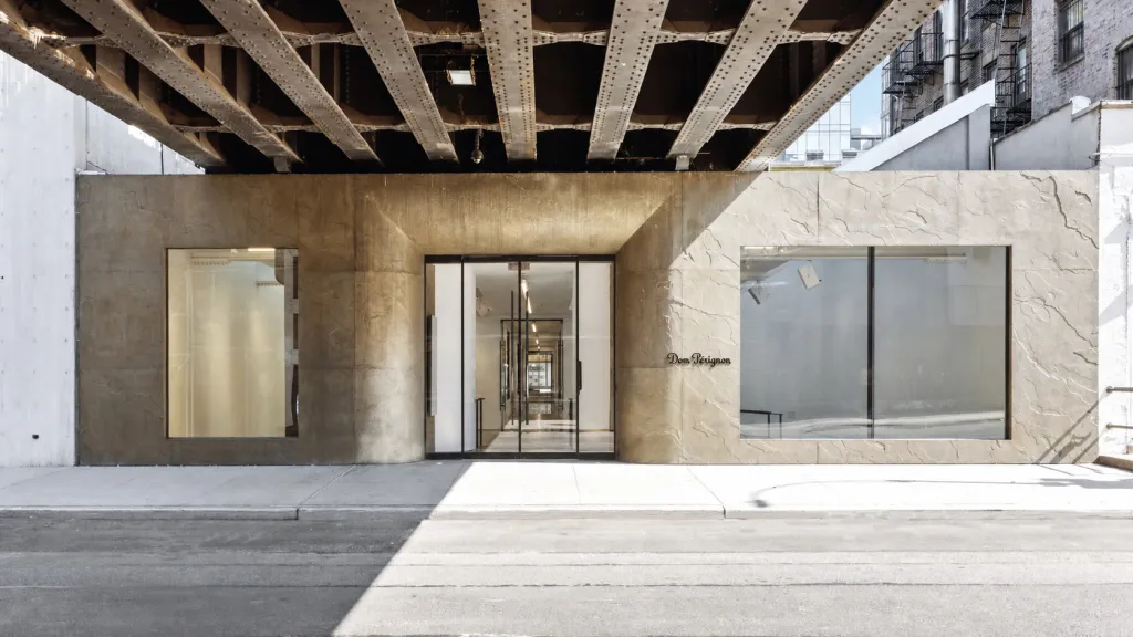 The entrance of the Dom Pérignon store, featuring a modern concrete facade with large glass windows and an overhead steel structure.