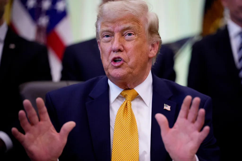 President Donald Trump speaks, with his hands raised, in the Oval Office.