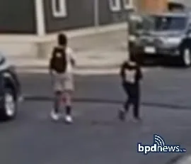 Two young people walking on a street, one with a backpack.