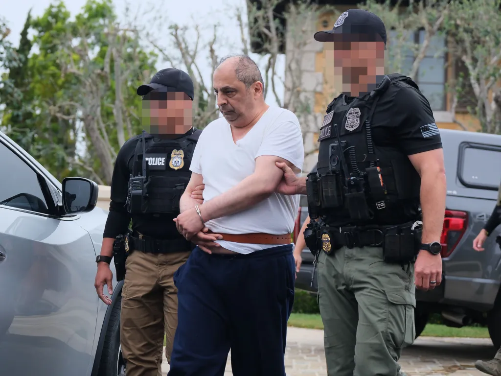 An arrested man in handcuffs being led by two police officers.