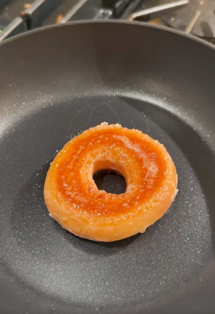 A glazed donut with a red/orange glaze in a non-stick frying pan.
