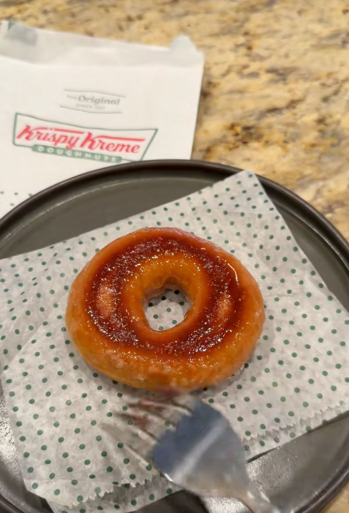 Krispy Kreme doughnut on a plate with a fork, and the brand's paper bag in the background.