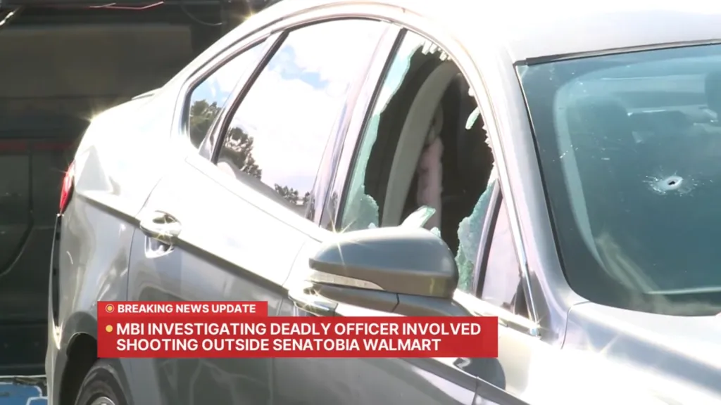 Damaged car with shattered windows and bullet hole, with a news chyron about an officer-involved shooting.