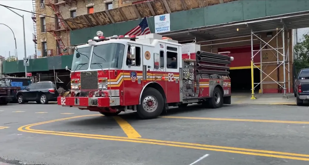 A red and white FDNY fire truck with unit number 82 driving out of a fire station.