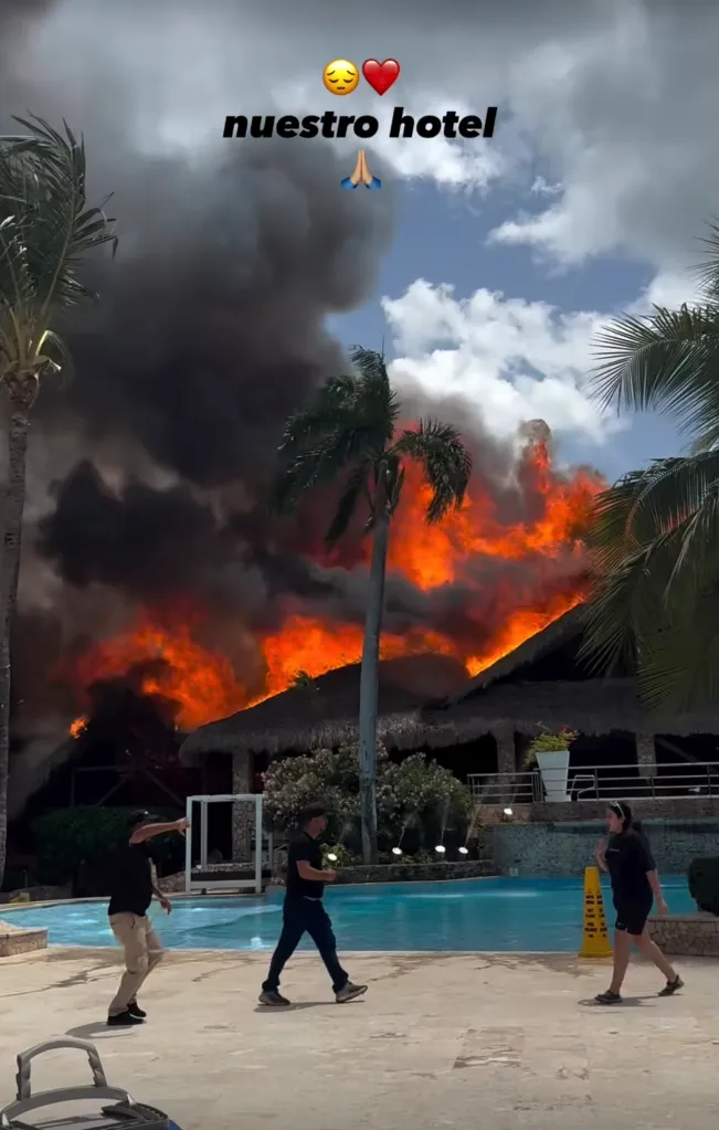 A building with a thatched roof engulfed in flames, with thick black smoke rising into the sky.