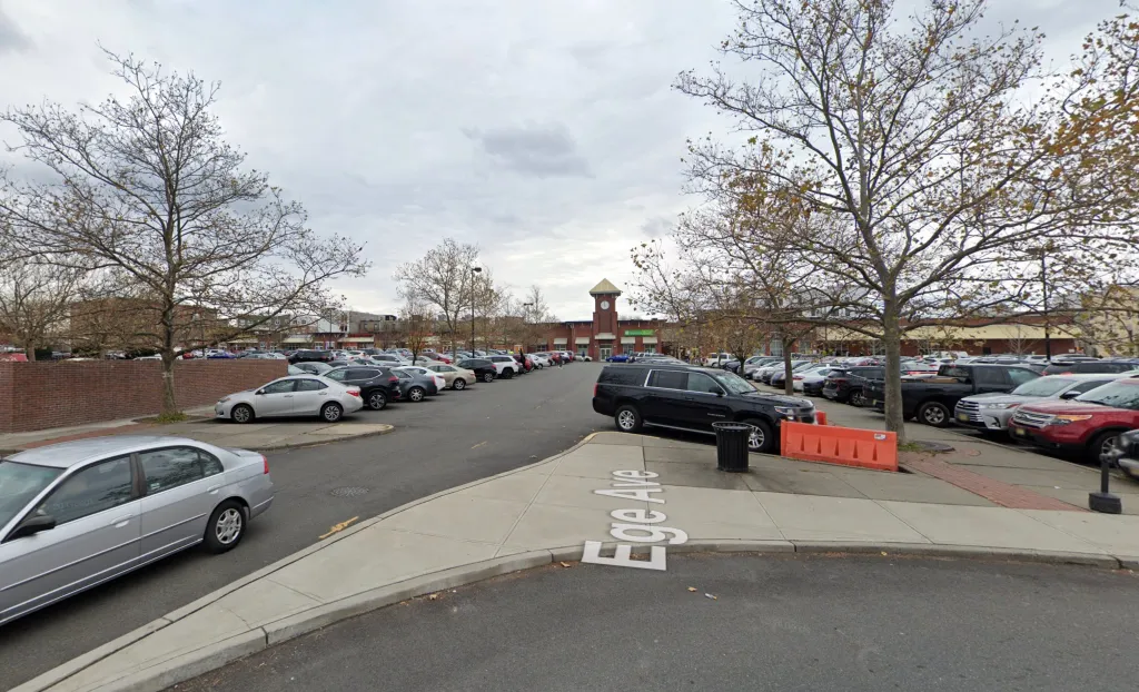 View of a shopping center parking lot with a red brick building with a clock tower and a sign for Ege Avenue in the foreground.