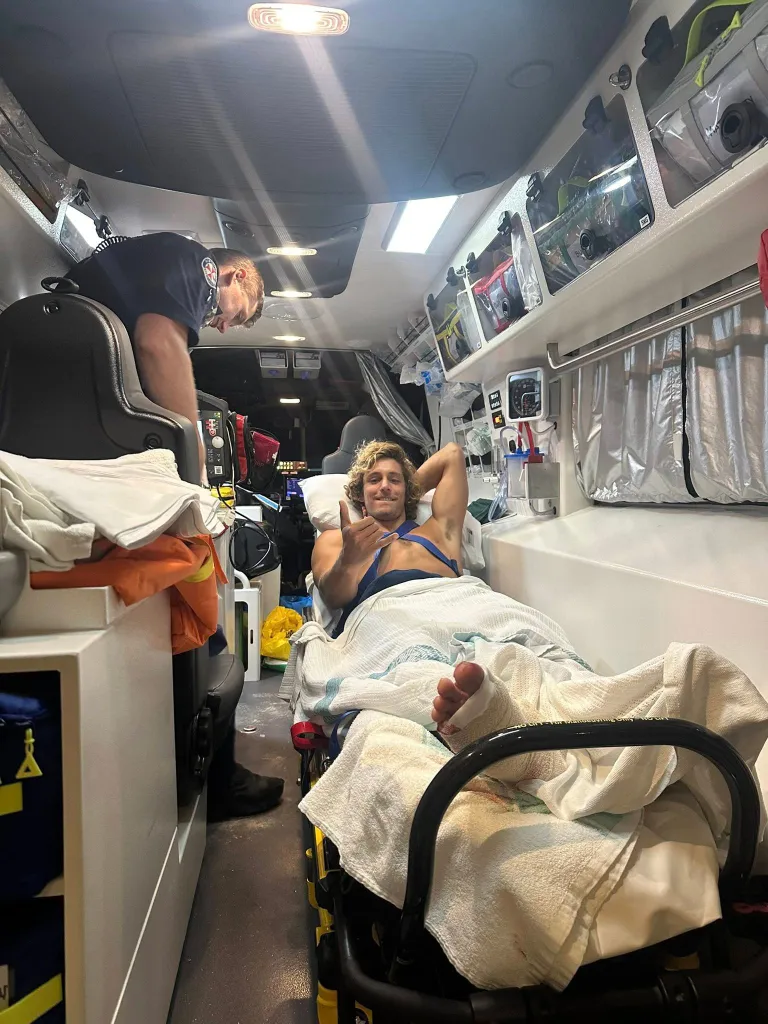 A man on an ambulance stretcher gives a thumbs-up to a paramedic.