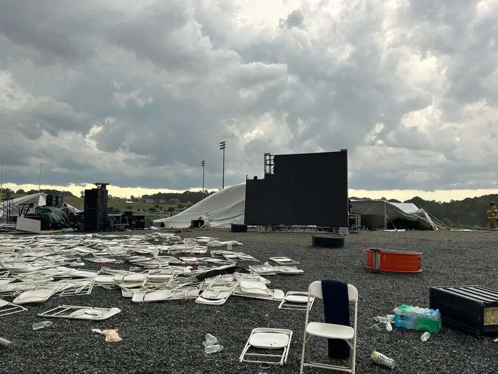 Damaged outdoor event space with overturned chairs, tents, and equipment under a cloudy sky.