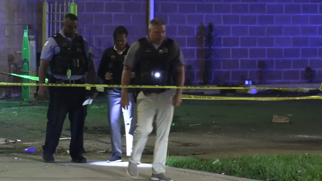 Two police officers walking behind crime scene tape at night.